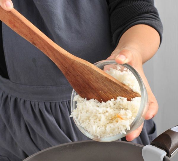 Chef vertiendo arroz cocido con una cuchara de madera en una sartén