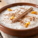 Arroz con leche espolvoreado con canela y con una ramita encima y cáscaras de limón