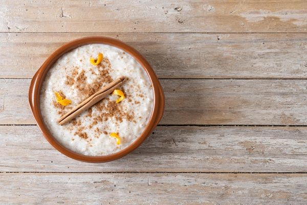 Arroz con leche espolvoreado con canela y con una ramita encima y cáscaras de limón vista desde arriba