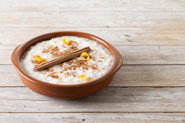 Arroz con leche espolvoreado con canela y con una ramita encima y cáscaras de limón vista de lado