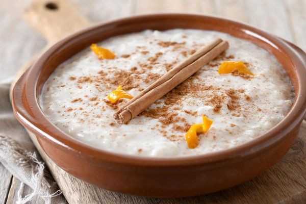 Arroz con leche espolvoreado con canela y con una ramita encima y cáscaras de limón