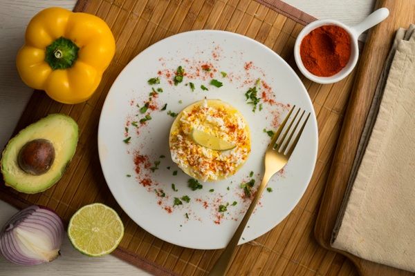Causa limeña tradicional peruana presentada en plato blanco con tenedor e ingredientes al lado vista desde arriba