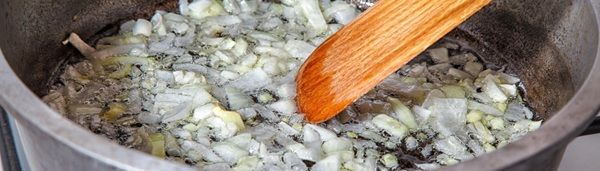 Cebolla friéndose en la sartén con pala de madera