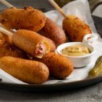 Corn dogs presentados sobre plato grande junto a mostaza