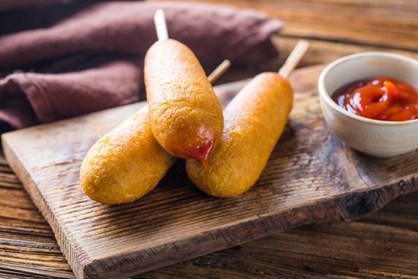 Corn dogs presentados sobre tabla de madera junto a un poco de ketchup