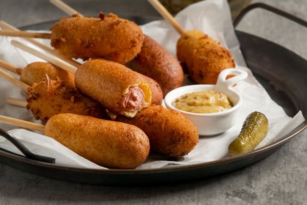 Corn dogs presentados sobre plato grande junto a mostaza