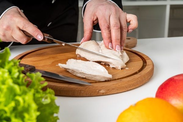 Chef cortando pollo cocido con cuchillo sobre tabla de madera