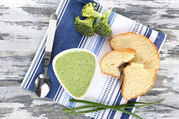 Crema de brócoli presentada en cuenco blanco sobre paño de cocina con cuchara y pan vista desde arriba