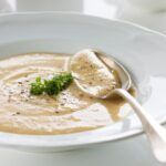 Crema de chirivías presentada en plato blanco con cuchara de metal y perejil por encima