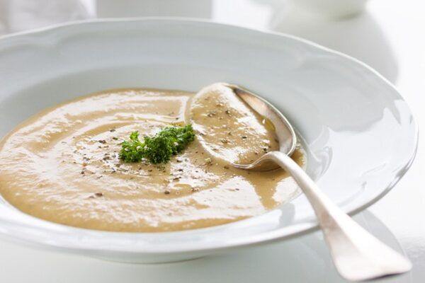 Crema de chirivías presentada en plato blanco con cuchara de metal y perejil por encima