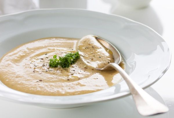 Crema de chirivías presentada en plato blanco con cuchara de metal y perejil por encima