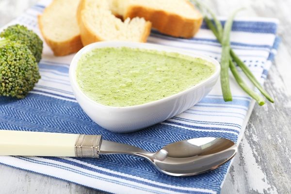 Crema de brócoli presentada en cuenco blanco sobre paño de cocina con cuchara y pan