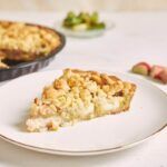 Porción de crumble de manzana en plato blanco y detrás la tarta