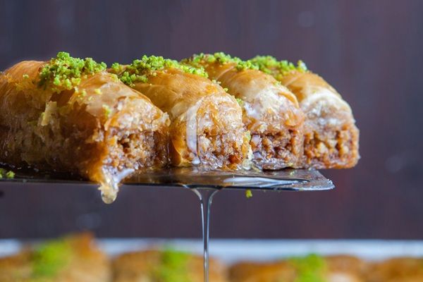 Dulces árabes sirviéndose con una espumadera de metal cayendo el almíbar por los lados