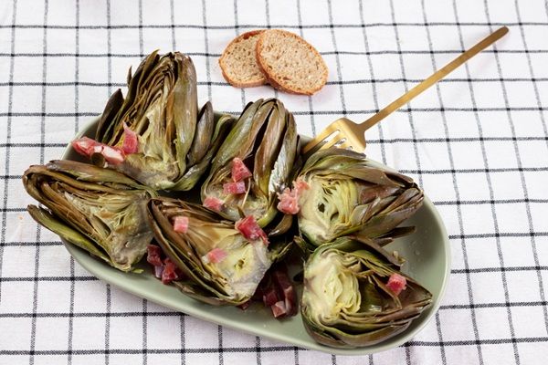 Flores de alcachofa con taquitos de jamón presentadas en bandeja junto a tenedor