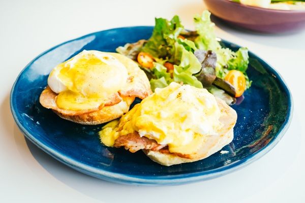 Huevos benedict con muffin inglés, jamón y salsa holandesa presentados en plato junto a ensalada