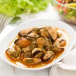Mejillones en escabeche presentados en plato blanco junto a tenedor, servilleta y ensalada