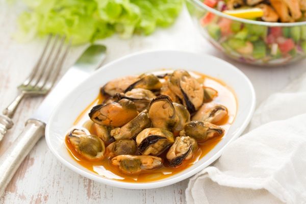 Mejillones en escabeche presentados en plato blanco junto a tenedor, servilleta y ensalada