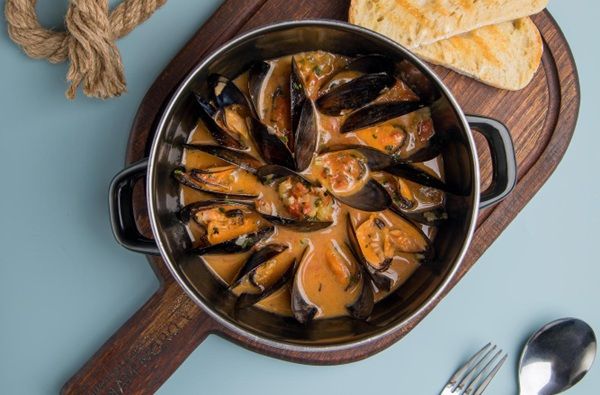 Mejillones a la marinera receta catalana presentados en sartén sobre tabla de madera junto a pan tostado