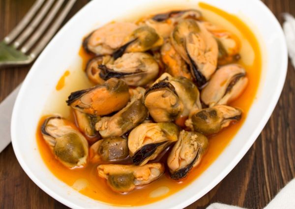 Mejillones en escabeche presentados en plato blanco junto a tenedor
