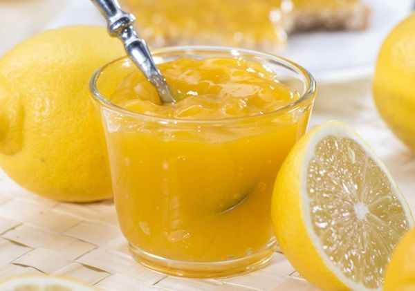 Mermelada de limón en tarro de cristal con cuchara dentro y limones cortados