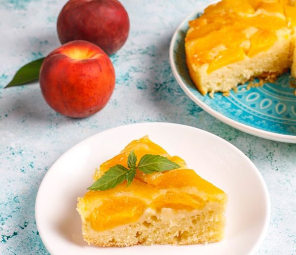 Porción de pastel de durazno presentado en plato blanco junto a duraznos