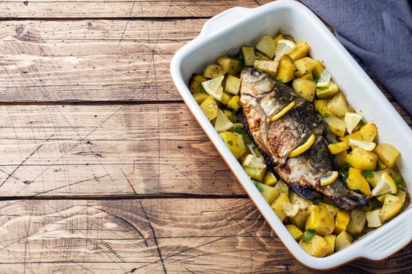 Besugo al horno con patatas presentado en bandeja blanca