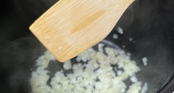 Cebolla picada haciéndose en una sartén con cuchara de madera