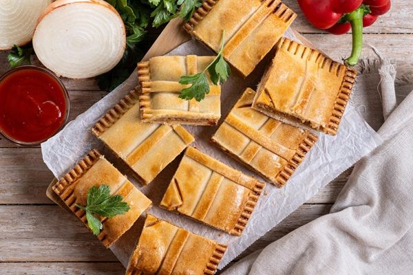 Empanada gallega de carne presentada sobre bandeja y cortada en trozos rectangulares vista desde arriba