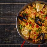 Paella mixta valenciana de pollo y verduras presentada en paellera sobre mesa de madera