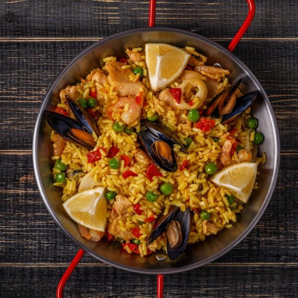 Paella mixta valenciana presentada en paellera sobre mesa de madera