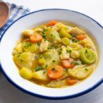 Porrusalda con bacalao presentada en plato hondo sobre paño y cuchara de madera al lado