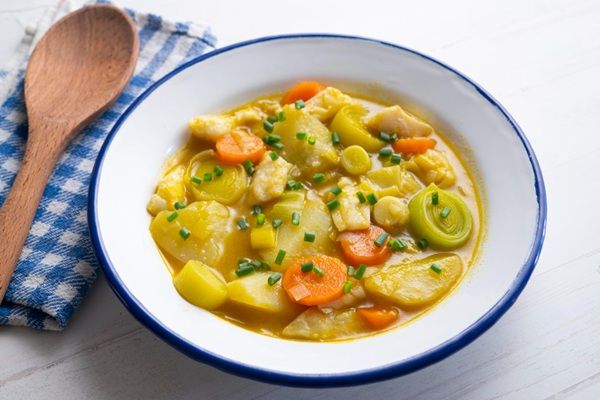 Porrusalda con bacalao presentada en plato hondo sobre paño y cuchara de madera al lado