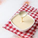 Bechamel casera en cuenco blanco sobre paño de cuadros rojos y blancos