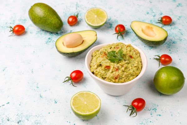 Guacamole casero mexicano presentado en cuenco blanco junto a ingredienes cortados