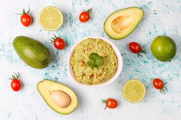 Guacamole casero mexicano presentado en cuenco blanco junto a ingredienes cortados vista desde arriba