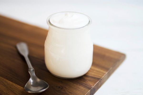 Vaso de yogurt junto a cuchara encima de una mesa de madera