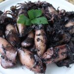 Chipirones en su tinta sobre plato blanco con perejil encima
