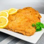 Wiener schnitzel o milanesa de ternera presentado en plato cuadrado blanco con rodajas de limón