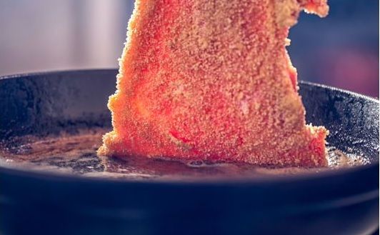 Wiener schnitzel o milanesa de ternera haciéndose en la sartén después de empanar