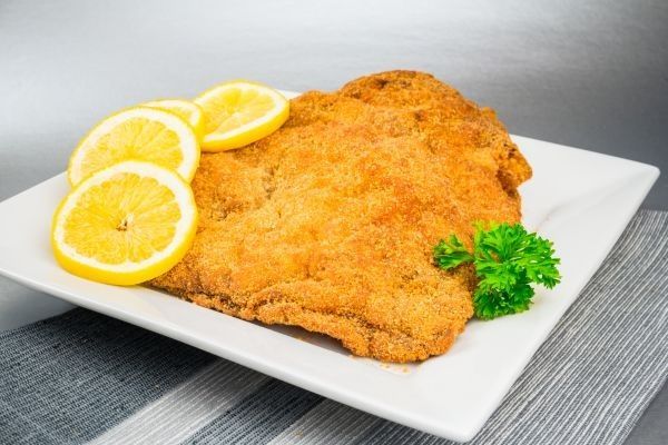 Wiener schnitzel o milanesa de ternera presentado en plato cuadrado blanco con rodajas de limón