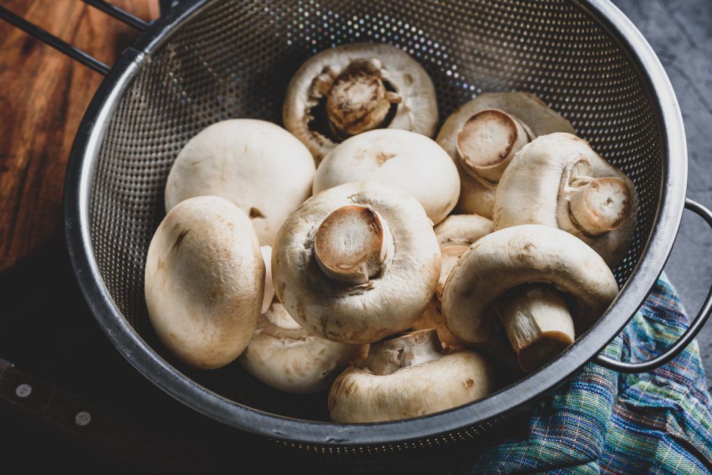 Button mushrooms in metal colander