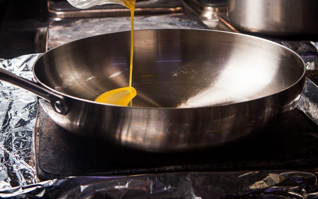 Side view pan with melted butter and human hand in stove on dark background