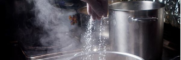 Chef echando sal marina en el agua de la olla