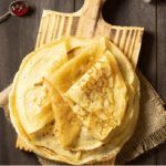 Filloas gallegas de leche presentadas en tabla de madera junto a cuchara con mermelada