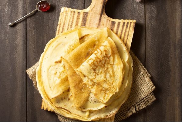 Filloas gallegas de leche presentadas en tabla de madera junto a cuchara con mermelada