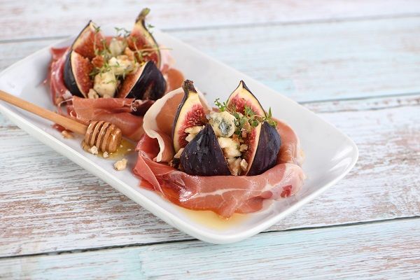 Figs wrapped in Parma ham Higos rellenos con queso azul envueltos en jamón y con miel presentados en planto blanco cuadrado