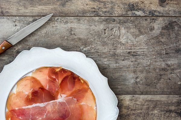 Lonchas de jamón serrano presentadas en plato blanco junto a cuchillo