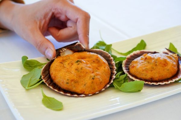 Vieiras rellenas con salsa de camarones, cebolla y pimientos presentadas sobre tabla blanca