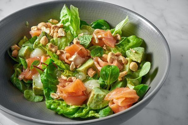 Ensalada fresca con salmón, queso suave, cacahuetes y menta vista desde el lado presentada en bol